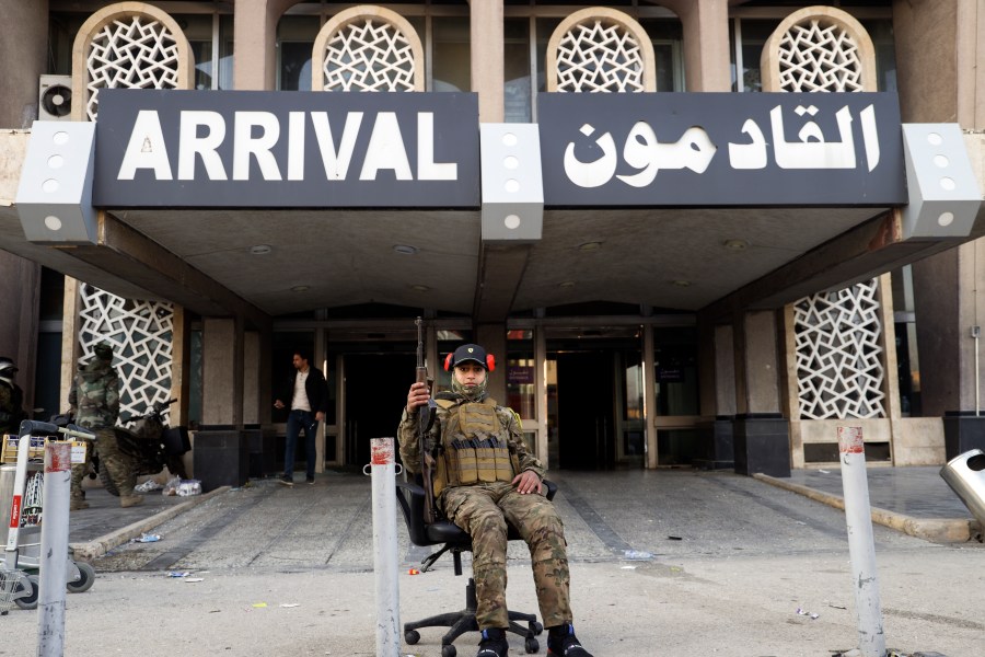 A Syrian opposition fighter sits on an office chair posing for a picture at arrivals gate of the Aleppo international airport in Aleppo, Syria, Monday, Dec. 2, 2024. .(AP Photo/Omar Albam)