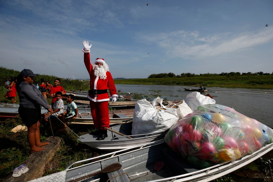 Jorge Barroso, dressed as Santa Claus, waves as he arrives on a boat to distribute Christmas gifts to children who live in the riverside communities of the Amazon, in Iranduba, Brazil, Saturday, Dec. 21, 2024. (AP Photo/Edmar Barros)